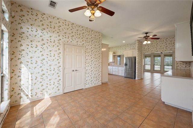 spare room with wallpapered walls, light tile patterned floors, baseboards, visible vents, and a ceiling fan