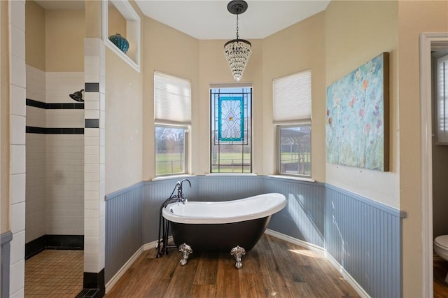 full bathroom featuring a walk in shower, toilet, wood finished floors, a soaking tub, and wainscoting