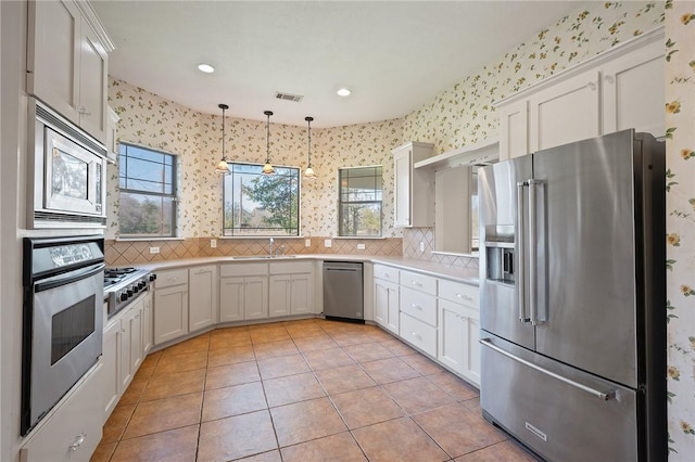 kitchen featuring stainless steel appliances, a sink, light countertops, tasteful backsplash, and wallpapered walls