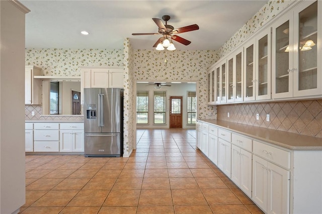 kitchen with glass insert cabinets, white cabinetry, light tile patterned flooring, high end refrigerator, and wallpapered walls