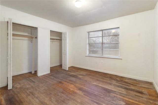 unfurnished bedroom featuring multiple closets and dark wood-type flooring