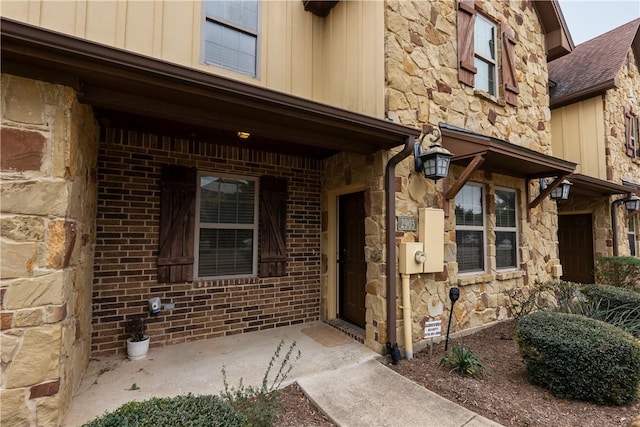 entrance to property with stone siding, board and batten siding, and roof with shingles