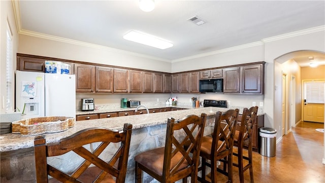 kitchen featuring white fridge with ice dispenser, black microwave, arched walkways, and light stone counters