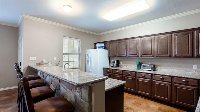 kitchen with crown molding, dark brown cabinets, light stone countertops, white fridge with ice dispenser, and a kitchen bar