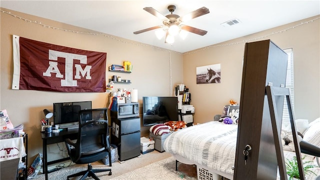 carpeted bedroom with ceiling fan, visible vents, and freestanding refrigerator