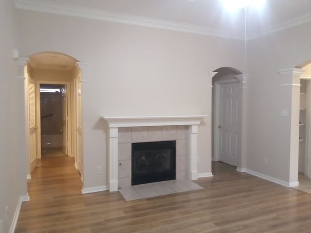 unfurnished living room featuring arched walkways, light wood-style flooring, ornamental molding, a tile fireplace, and ornate columns