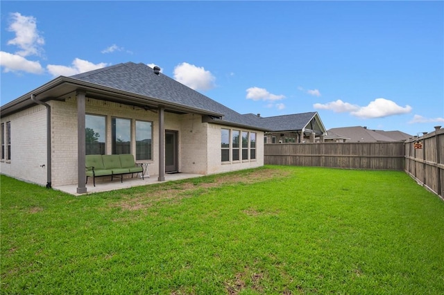 rear view of property with brick siding, a fenced backyard, a yard, a patio, and a shingled roof