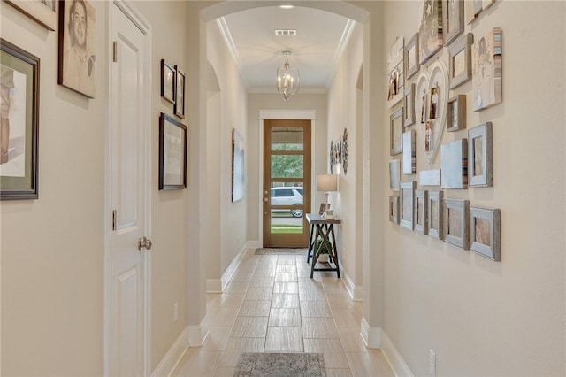corridor with visible vents, ornamental molding, baseboards, arched walkways, and a notable chandelier