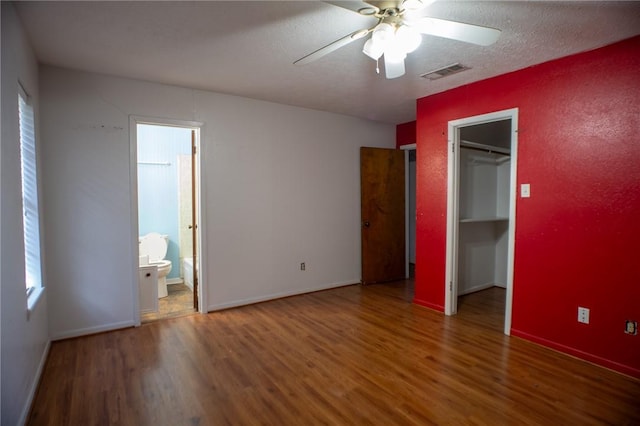 unfurnished bedroom featuring ensuite bathroom, a walk in closet, a textured ceiling, dark hardwood / wood-style floors, and ceiling fan