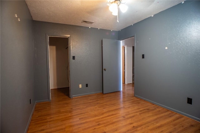 unfurnished bedroom with a closet, a spacious closet, hardwood / wood-style floors, and a textured ceiling