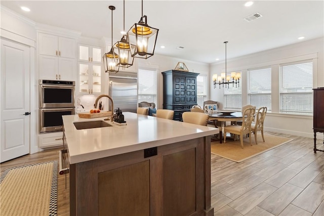 kitchen with a notable chandelier, light countertops, glass insert cabinets, appliances with stainless steel finishes, and white cabinetry