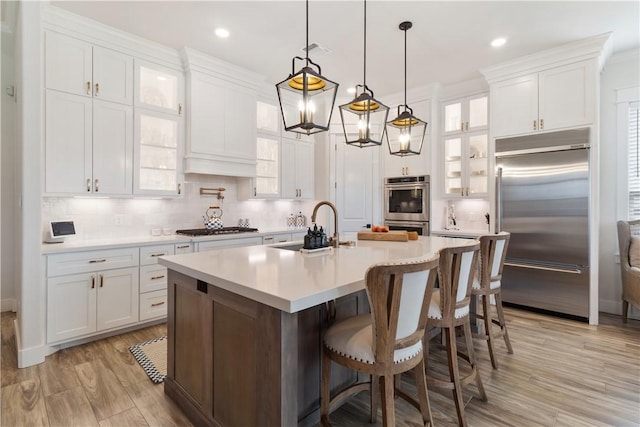 kitchen featuring stainless steel appliances, a sink, white cabinets, light countertops, and glass insert cabinets