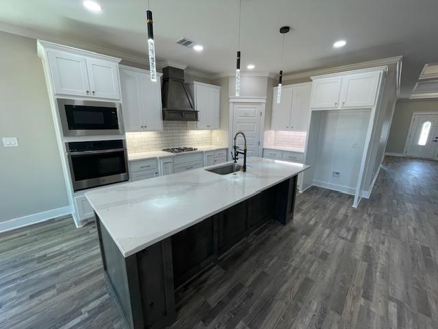 kitchen featuring premium range hood, sink, a center island with sink, stainless steel appliances, and white cabinets