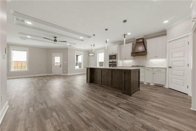 2908 Goldberg Dr, Bryan, TX 77808 - kitchen with premium range hood, stainless steel microwave, wood finished floors, baseboards, and tasteful backsplash