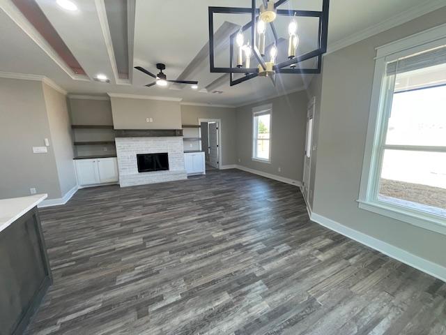 unfurnished living room with ornamental molding, dark hardwood / wood-style floors, ceiling fan with notable chandelier, and a fireplace