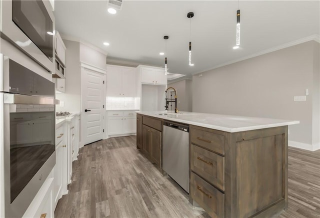 2908 Goldberg Dr, Bryan, TX 77808 - kitchen featuring appliances with stainless steel finishes, ornamental molding, white cabinets, an island with sink, and a sink