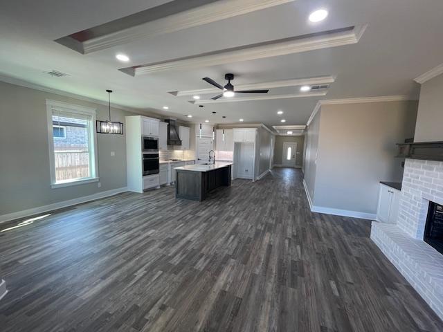 unfurnished living room featuring a brick fireplace, crown molding, dark wood-type flooring, and ceiling fan