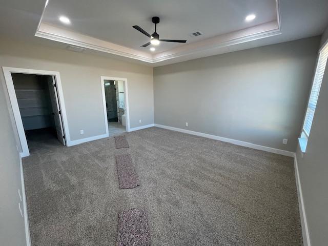 unfurnished bedroom with dark colored carpet, a spacious closet, ensuite bathroom, and a tray ceiling