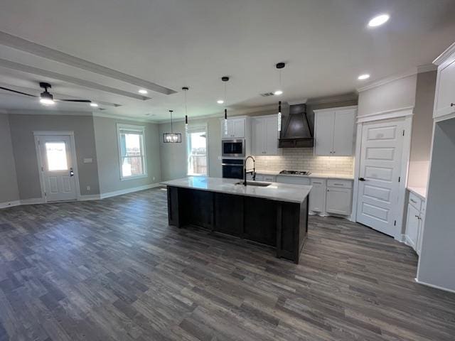 kitchen with pendant lighting, stainless steel appliances, custom range hood, white cabinets, and a center island with sink