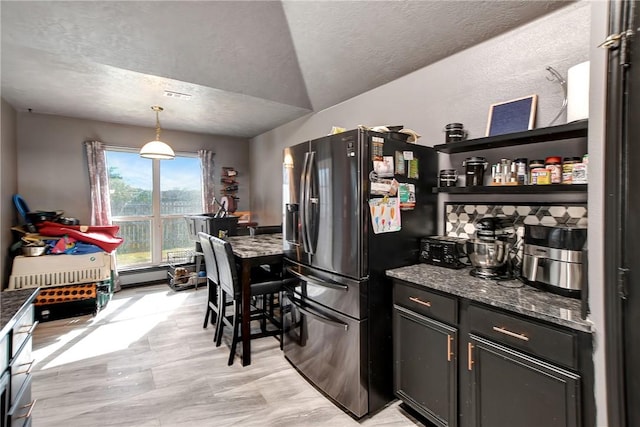 kitchen featuring pendant lighting, lofted ceiling, dark stone countertops, a baseboard radiator, and stainless steel fridge with ice dispenser