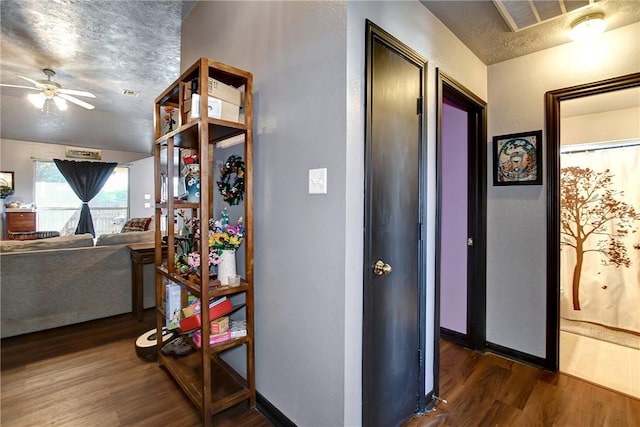 hallway with a textured ceiling, dark wood-type flooring, and vaulted ceiling