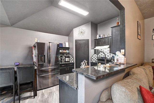 kitchen featuring kitchen peninsula, stainless steel refrigerator with ice dispenser, decorative backsplash, and lofted ceiling