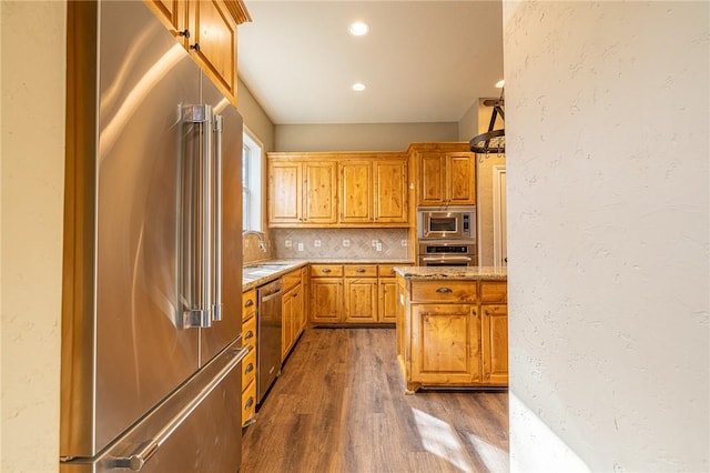 kitchen featuring dark wood finished floors, a sink, appliances with stainless steel finishes, a textured wall, and backsplash