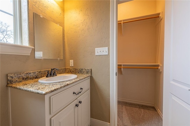 bathroom with vanity, a walk in closet, baseboards, and a textured wall