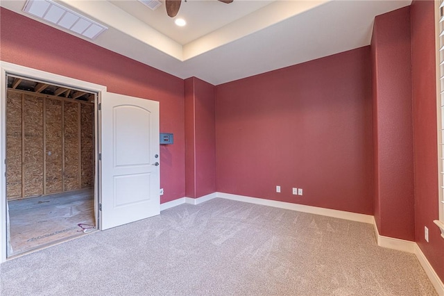 carpeted empty room featuring a raised ceiling, baseboards, visible vents, and ceiling fan