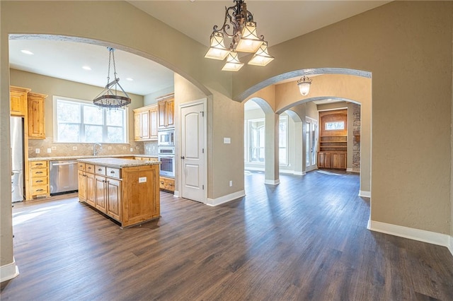 kitchen with tasteful backsplash, baseboards, dark wood finished floors, appliances with stainless steel finishes, and arched walkways