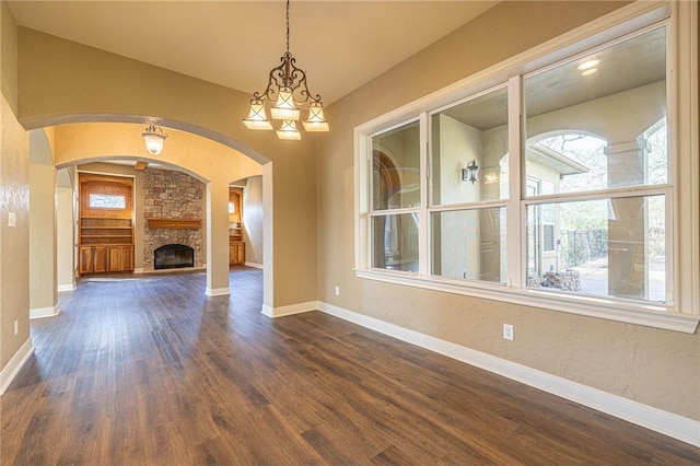 unfurnished living room featuring dark wood finished floors, arched walkways, a fireplace, baseboards, and a textured wall