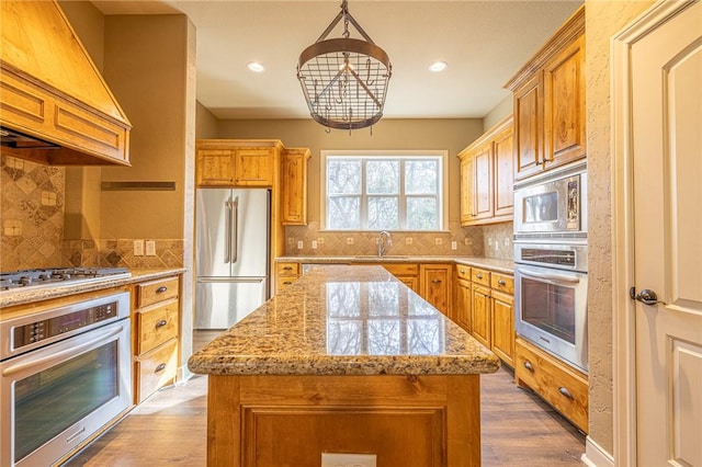 kitchen with light stone countertops, premium range hood, dark wood-style flooring, a sink, and appliances with stainless steel finishes