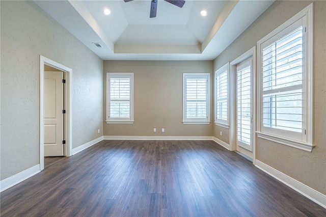 empty room with a raised ceiling, a ceiling fan, dark wood-type flooring, and baseboards