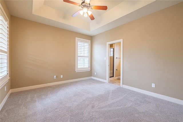 empty room with a tray ceiling, baseboards, light colored carpet, and ceiling fan