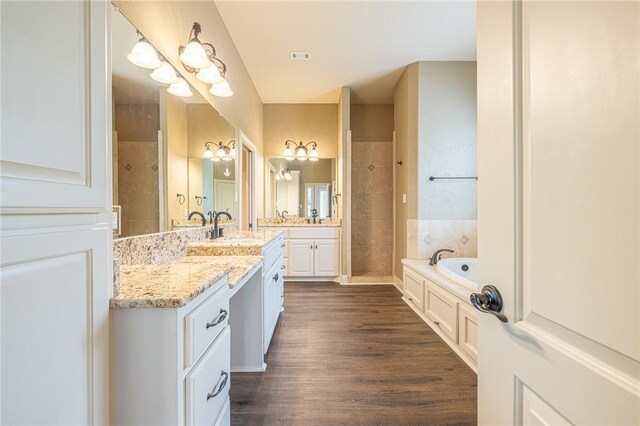 bathroom featuring vanity, wood finished floors, tiled shower, an inviting chandelier, and a bath