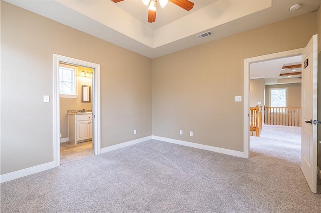 unfurnished room featuring visible vents, light carpet, a raised ceiling, a ceiling fan, and baseboards