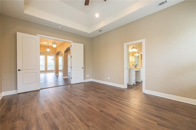 unfurnished bedroom with visible vents, baseboards, dark wood finished floors, arched walkways, and a raised ceiling