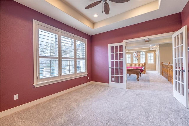 carpeted empty room featuring french doors, baseboards, a raised ceiling, and a ceiling fan