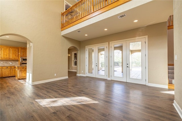 unfurnished living room with visible vents, dark wood-style floors, arched walkways, baseboards, and a towering ceiling