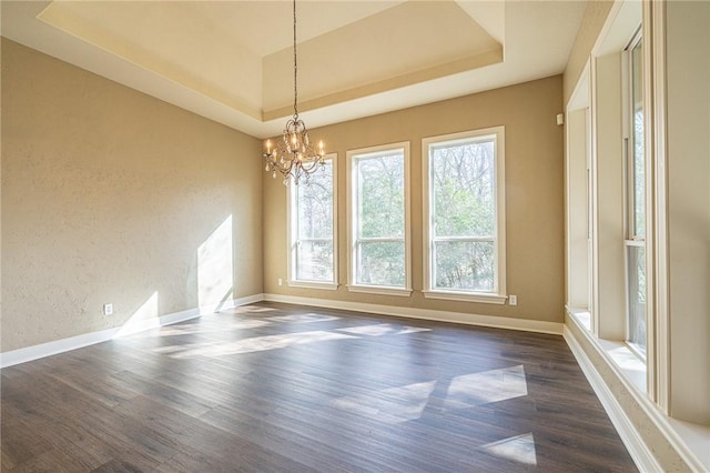 empty room featuring a raised ceiling, a notable chandelier, dark wood finished floors, baseboards, and a textured wall