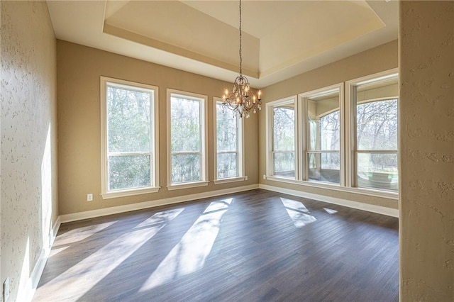 unfurnished dining area featuring a raised ceiling, a notable chandelier, dark wood finished floors, baseboards, and a textured wall