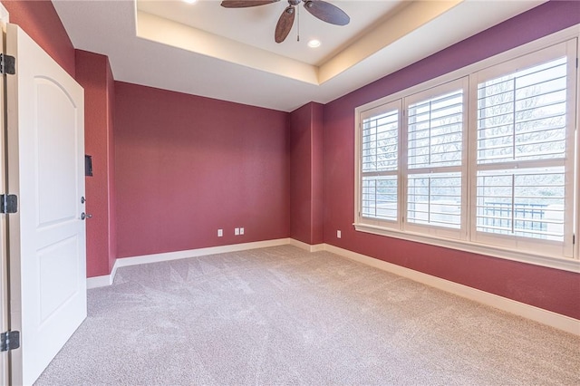 carpeted empty room with a tray ceiling, baseboards, and ceiling fan