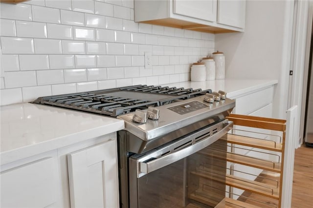 kitchen with stainless steel gas stove, tasteful backsplash, white cabinets, and light wood-type flooring