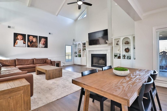 living room featuring hardwood / wood-style floors, a towering ceiling, beamed ceiling, a premium fireplace, and ceiling fan