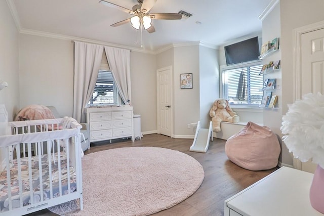 bedroom with ceiling fan, a nursery area, dark hardwood / wood-style flooring, and ornamental molding