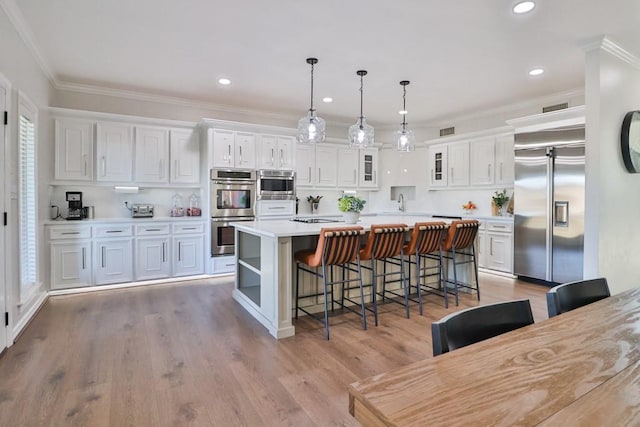 kitchen with a breakfast bar area, appliances with stainless steel finishes, hanging light fixtures, white cabinets, and a center island