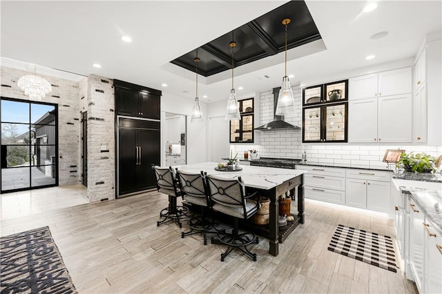 kitchen featuring light stone counters, hanging light fixtures, backsplash, paneled built in refrigerator, and wall chimney exhaust hood