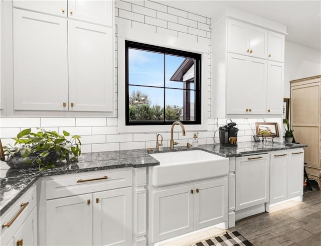 kitchen with wood finished floors, backsplash, a sink, and white cabinetry