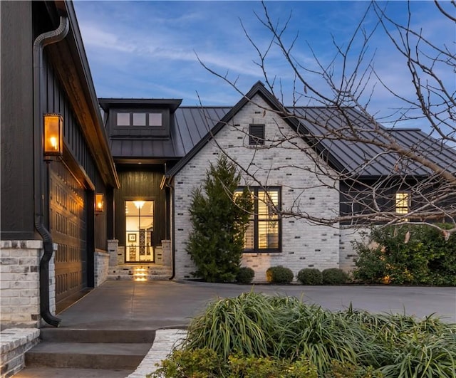 view of front of home featuring metal roof, brick siding, a standing seam roof, and driveway