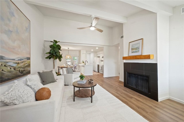 2800 Longmire Dr Unit 22, College Station, TX 77845 - living room with light wood-type flooring, a tiled fireplace, a ceiling fan, baseboards, and beamed ceiling